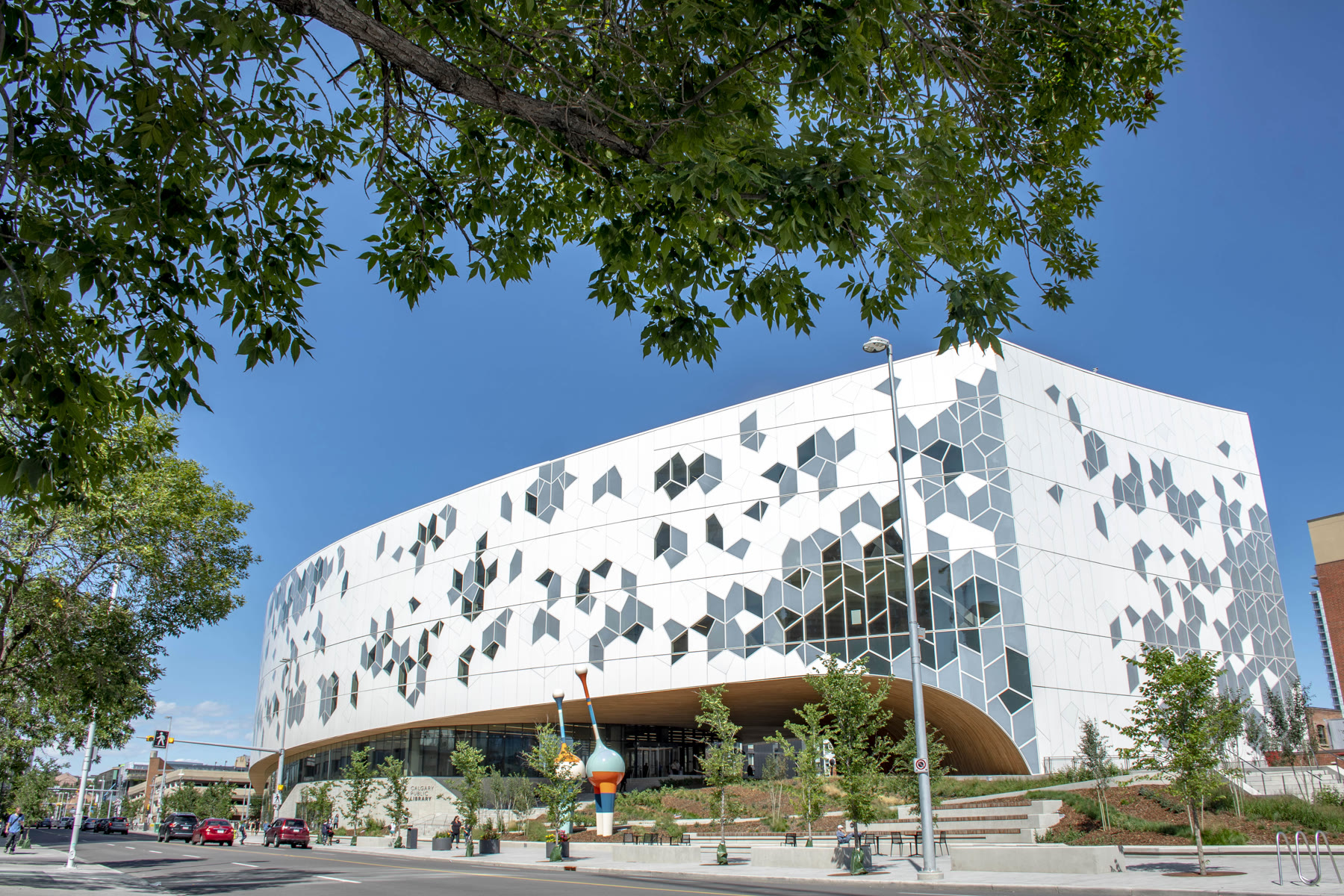 The geometric facade of Calgary Central Library framed by trees
